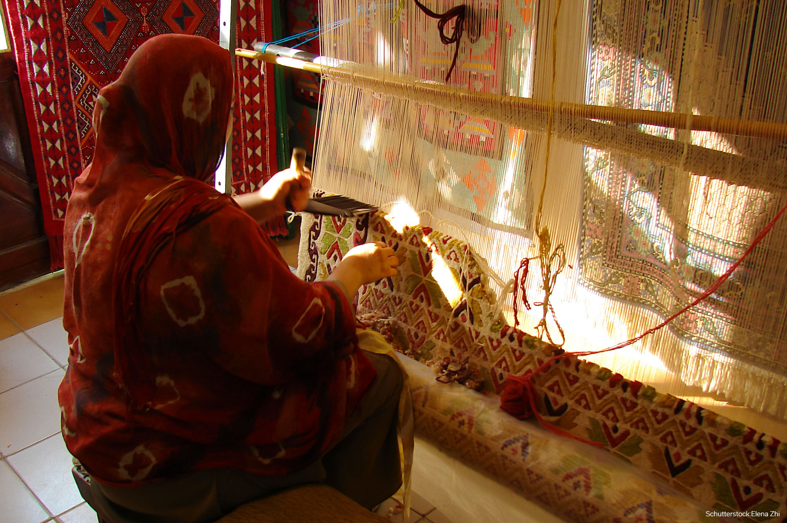 a diligent woman in national clothes makes a colorful traditional woolen carpet by hand, a pile rug, an oriental ornament, side view, Tunisia;